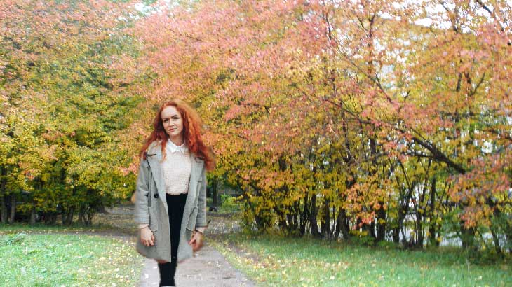 Рыжая девушка на фоне осенних деревьев.
